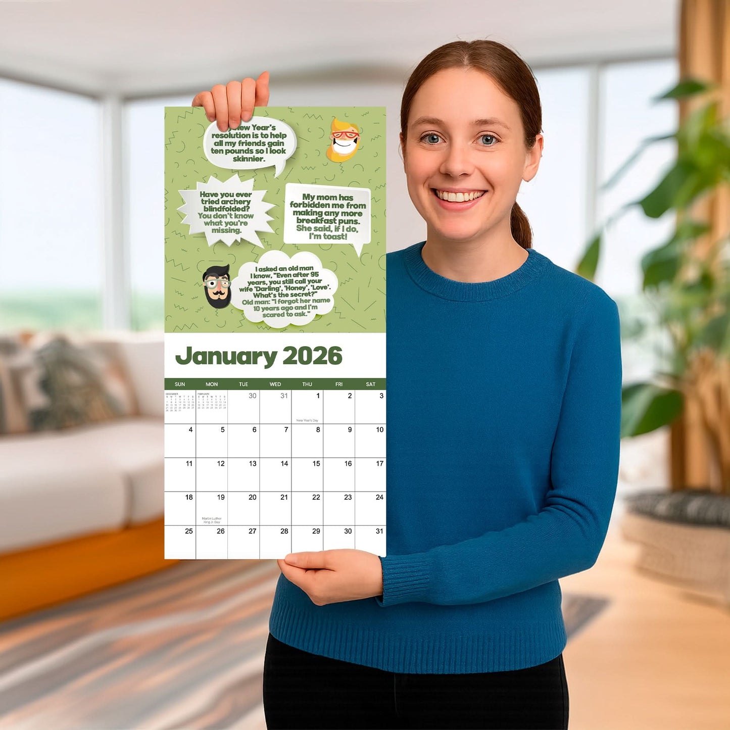 A woman in a blue sweater stands indoors, smiling as she holds up the 2026 Dad Joke Wall Calendar by That Is So Dad, featuring cartoon animals and dad jokes in speech bubbles for January 2026.