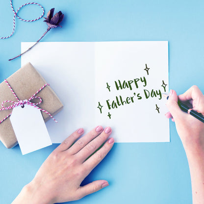 Someone writes "Happy Father's Day" inside the Funny Father's Day Card "This Is Not A Drill" by That Is So Dad, on a blue background, beside a wrapped gift with a white tag.