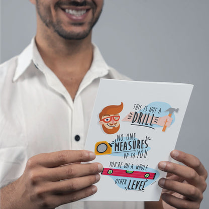 A man in a white shirt holds the "This Is Not A Drill" Funny Father's Day Card by That Is So Dad, featuring playful illustrations and the message, "No one measures up to you. You're on a whole other level." Perfect for Father’s Day.