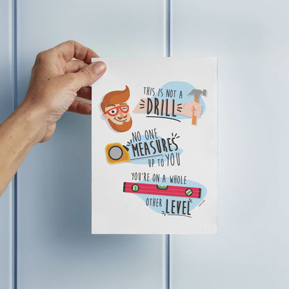 A hand holds the "This Is Not A Drill" funny Father's Day card by That Is So Dad, featuring cartoon tools and the message: "No one measures up to you. You're on a whole other level." Ideal for Father’s Day appreciation.