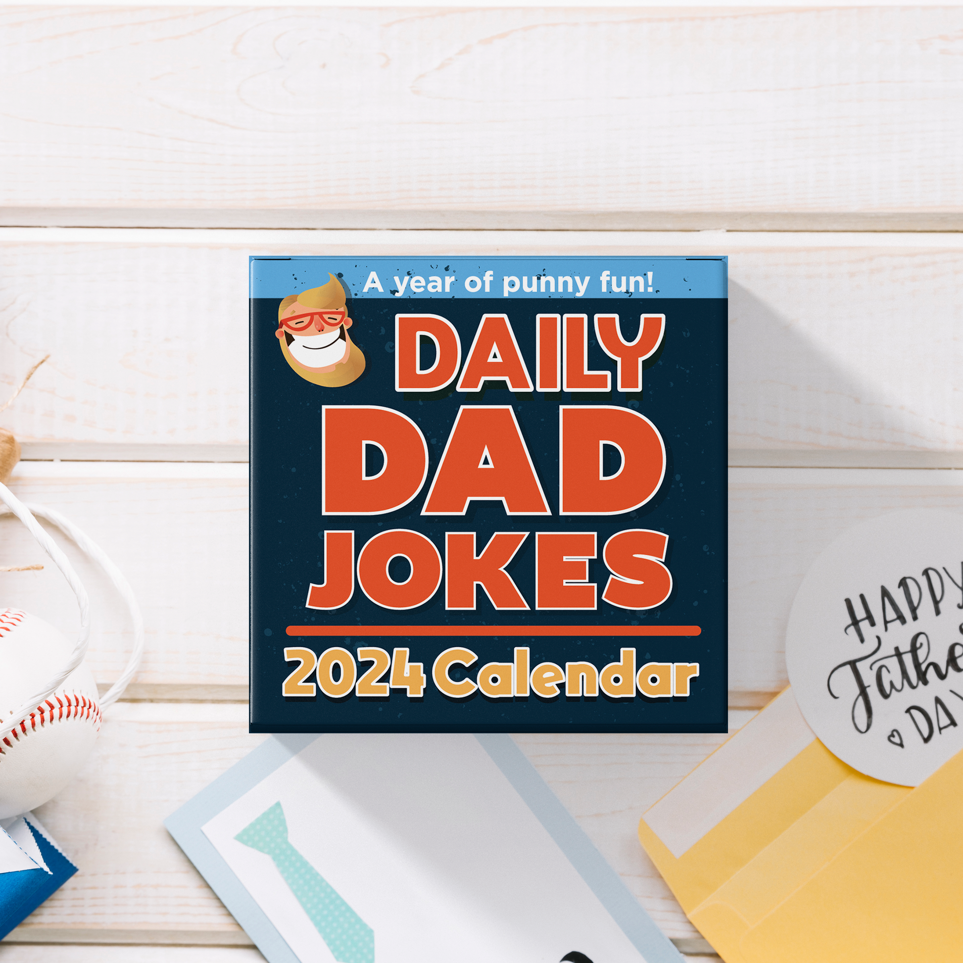 A day-to-day calendar titled "2024 Dad Joke Calendar - Day to Day Jokes!" by That Is So Dad is placed on a wooden surface, accompanied by greeting cards, an envelope, and a baseball.